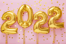 gold balloons in the shape of the year 2022 on a pink background