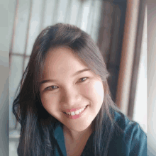 a woman with long black hair is smiling and wearing a blue shirt