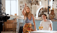 a woman in a crop top stands in front of a man sitting at a table with glasses of beer