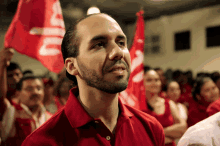 a man in a red shirt stands in front of a crowd holding a flag that says ' cia ' on it