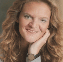 a woman with a watch on her wrist smiles with her hand on her face