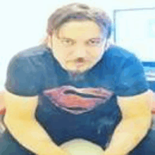 a man wearing a superman t-shirt is sitting down with his hands folded .