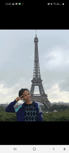 a girl stands in front of the eiffel tower giving a peace sign