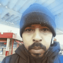 a man with a beard wears a blue beanie and a black hoodie