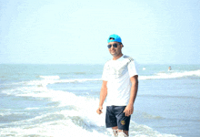 a man wearing a blue hat and sunglasses is standing in the ocean