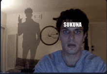 a man is sitting in front of a shadow of a man with the word sukuna on his head