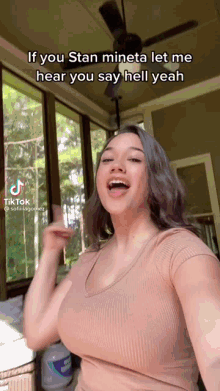 a woman in a tan top is standing in front of a screened in porch with a ceiling fan .