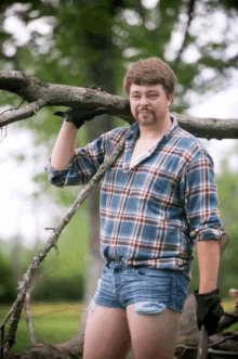 a man wearing shorts and a plaid shirt holds a tree branch over his head