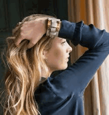 a woman wearing a blue shirt and a watch is looking out a window .