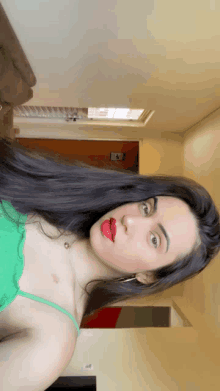 a woman wearing a green top and red lipstick takes a selfie