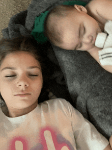 a girl laying next to a baby wearing a t-shirt that says ' a ' on it