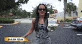 a woman wearing sunglasses is standing in a parking lot with a stop sign in the background and a sign that says earlier today