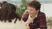 a young man with curly hair is sitting at a table with a bottle of orange juice in front of him .