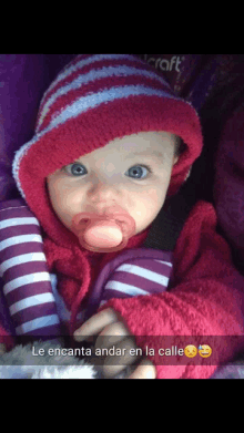 a baby with a pacifier in her mouth is wearing a red hat and purple striped pants