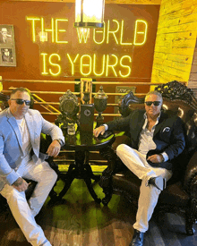 two men sit in front of a sign that says the world is yours