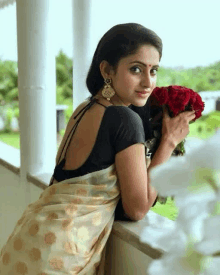 a woman in a saree and black blouse is holding a bouquet of roses .