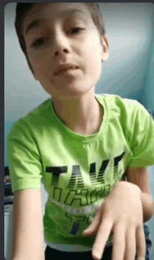 a young boy wearing a green t-shirt with the word take on it is making a funny face .