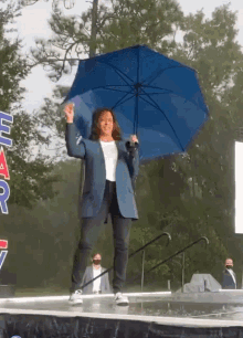 a woman holding a blue umbrella stands on a stage in front of a sign that says " har "