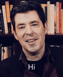 a man is smiling in front of a bookshelf and the word hi is on his shirt