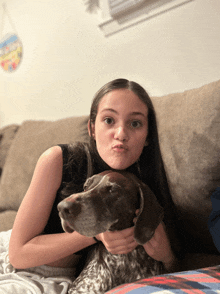 a girl sitting on a couch holding a dog and making a funny face