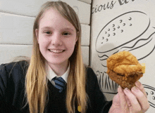 a girl is holding a piece of fried chicken in front of a wall that says delicious