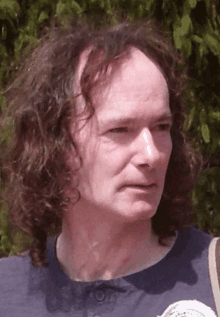 a man with long curly hair is wearing a blue shirt with a white emblem on the front