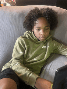 a young boy wearing a green nike sweatshirt sits on a chair