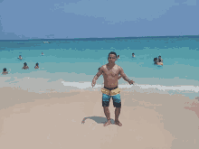 a shirtless man stands on the beach giving a peace sign