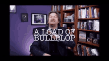 a man in a suit is sitting in front of a bookshelf with the words a load of bullplop above him .