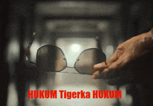 a person is holding a pair of sunglasses with the words hukum tigerka hukum written below them