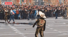 a man in a mariachi outfit is standing in front of a crowd and a sign that says en vivo