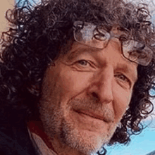 a close up of a man with curly hair and glasses smiling .