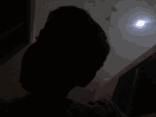 a silhouette of a person in a dark room with a light shining through the ceiling