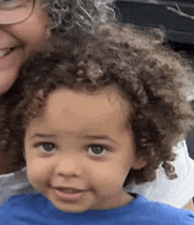 a little boy with curly hair is sitting next to a woman and smiling .