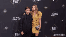 a man and woman are posing for a picture in front of a wall that says the people have spoken