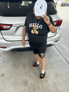 a woman wearing a hello teddy bear shirt stands in front of a car