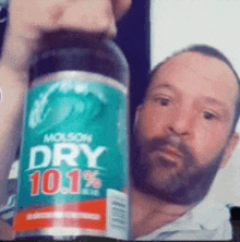 a man with a beard is holding up a bottle of molson dry beer .