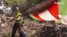 a man in a green shirt is standing in the woods with a red white and green flag flying in the background