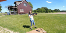 a woman holding a rifle in front of a brown house