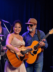 a man and a woman are holding guitars on a stage