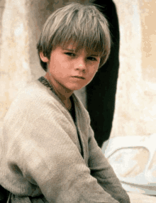 a young boy with blonde hair is wearing a grey sweater