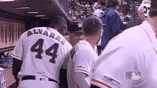 a group of baseball players are standing in a dugout and one of them has the number 44 on his back .