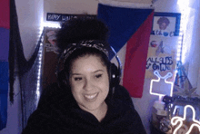 a woman wearing headphones and a bandana is smiling in front of a flag .