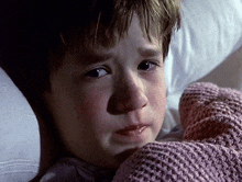 a young boy is laying in bed with a pink blanket covering him