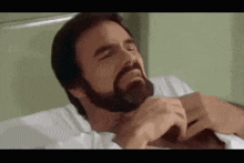 a man with a beard is laying in a hospital bed holding his chest .