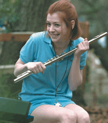 a girl in a blue shirt is holding a flute and smiling