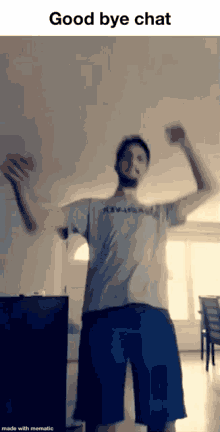 a man in a gray shirt and blue shorts is dancing in a living room with his arms in the air .