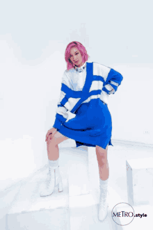 a woman with pink hair is wearing a blue and white sweater and white boots