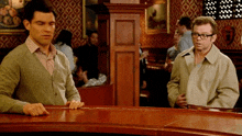 two men are standing at a bar in a bar .