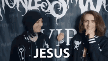 two men are standing in front of a wall that says jesus